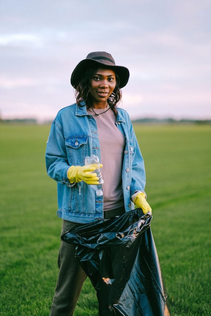 woman-in-blue-denim-jacket-holding-a-plastic-bottle-and-black-plastic-bag-5029852 A woman in a denim jacket collecting trash in a green field, promoting volunteer work.